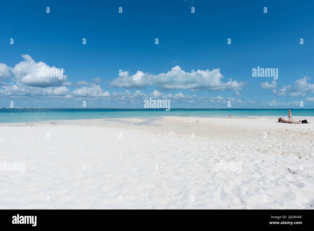 Young mother tans on the beach as young son runs in the sand during summer vacation in Isla Mujeres, Mexico Stock Photo