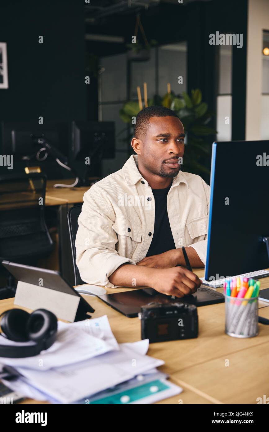 Young Black Male Advertising Marketing Or Design Creative In Modern Office Sitting At Desk Working On Computer Portrait Stock Photo