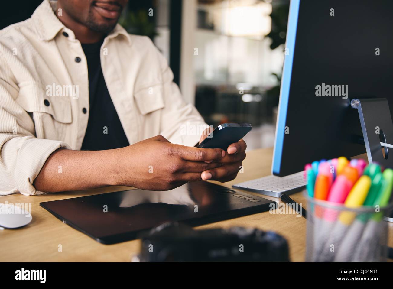 Close Up Anonymous Young Black Male Creative In Modern Office Sitting At Desk Using Mobile Phone Stock Photo