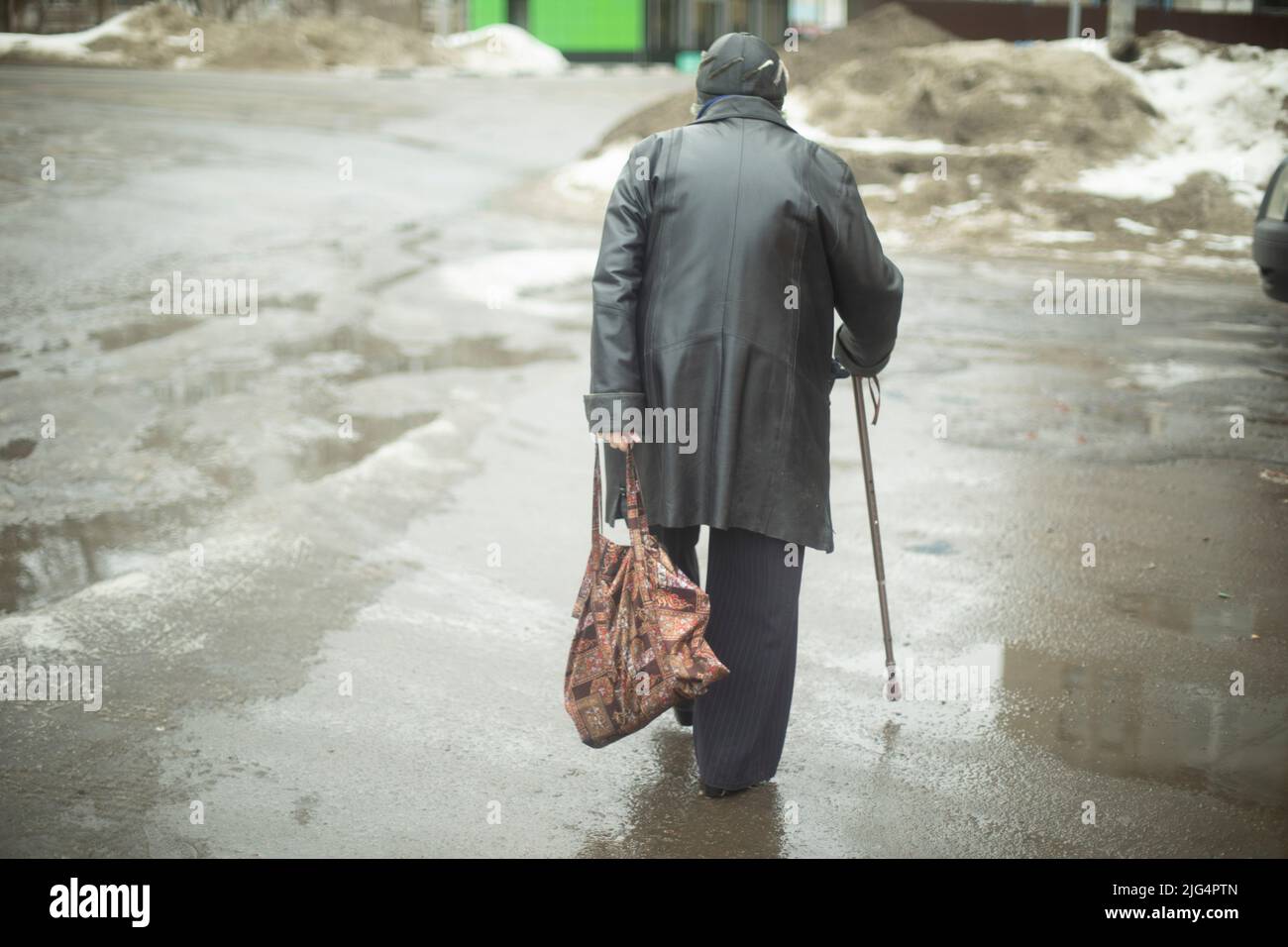 Woman with pore stick walks down street while walking. Pensioner in Russia. Old woman walks with bag in her hand. Stock Photo