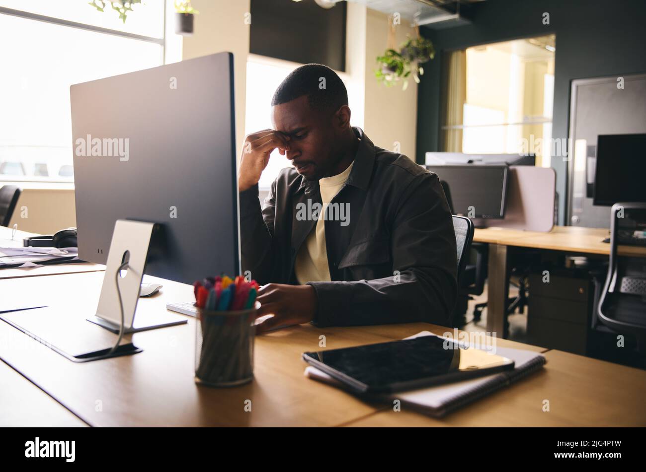 Stressed black businessman sat at office desk with mental illness Stock Photo