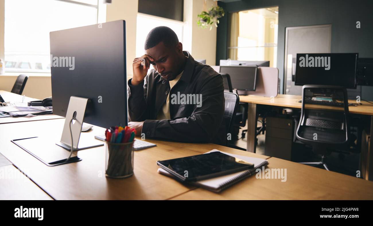 Depressed black businessman sat at office desk with mental health issues Stock Photo