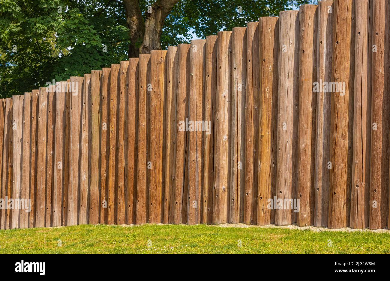 Wooden fence posts, round wood. Wooden wall from logs a strong protection in ancient times. Round timber wood fence. Street photo, nobody, travel phot Stock Photo