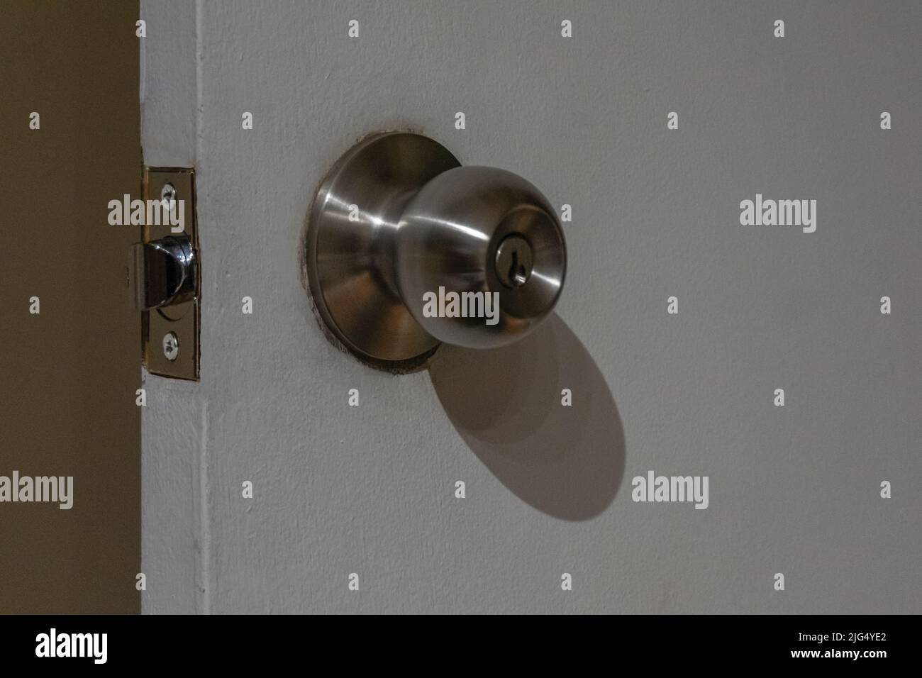 Close view of a round stainless steel door knob on a white wooden door. Door open. Stock Photo