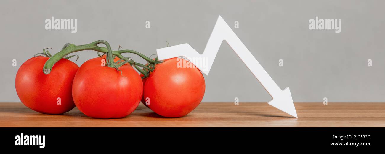 The price of tomatoes and vegetables. Bad vegetable harvest. Fresh red ripe tomatoes with twigs on the table. Graph chart points down. Stock Photo