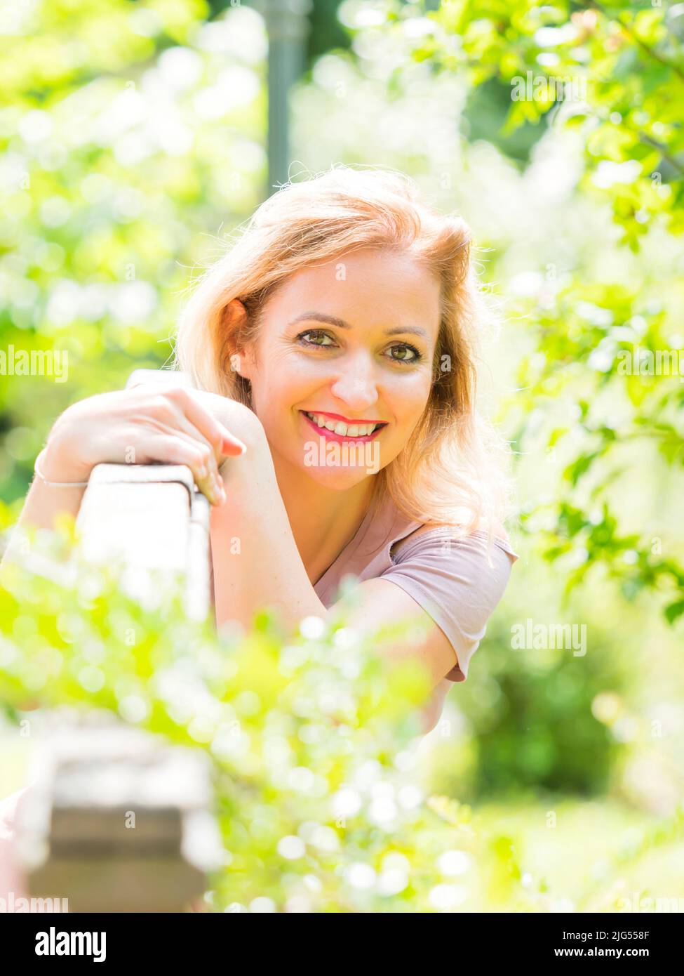 Blonde hair woman 30s portrait high-hey brigts light sunshine sunlight very sunny happy in park looking smiling at camera isolated focus bokeh Stock Photo