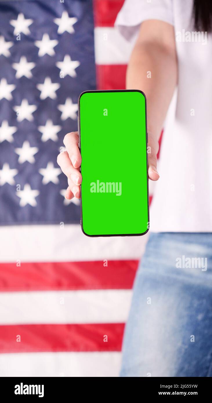 Hand holding mobile phone with green screen United states of America flag on background. Mockup phone. Labor day, 4th of July, Memorial day, 9.11. Stock Photo