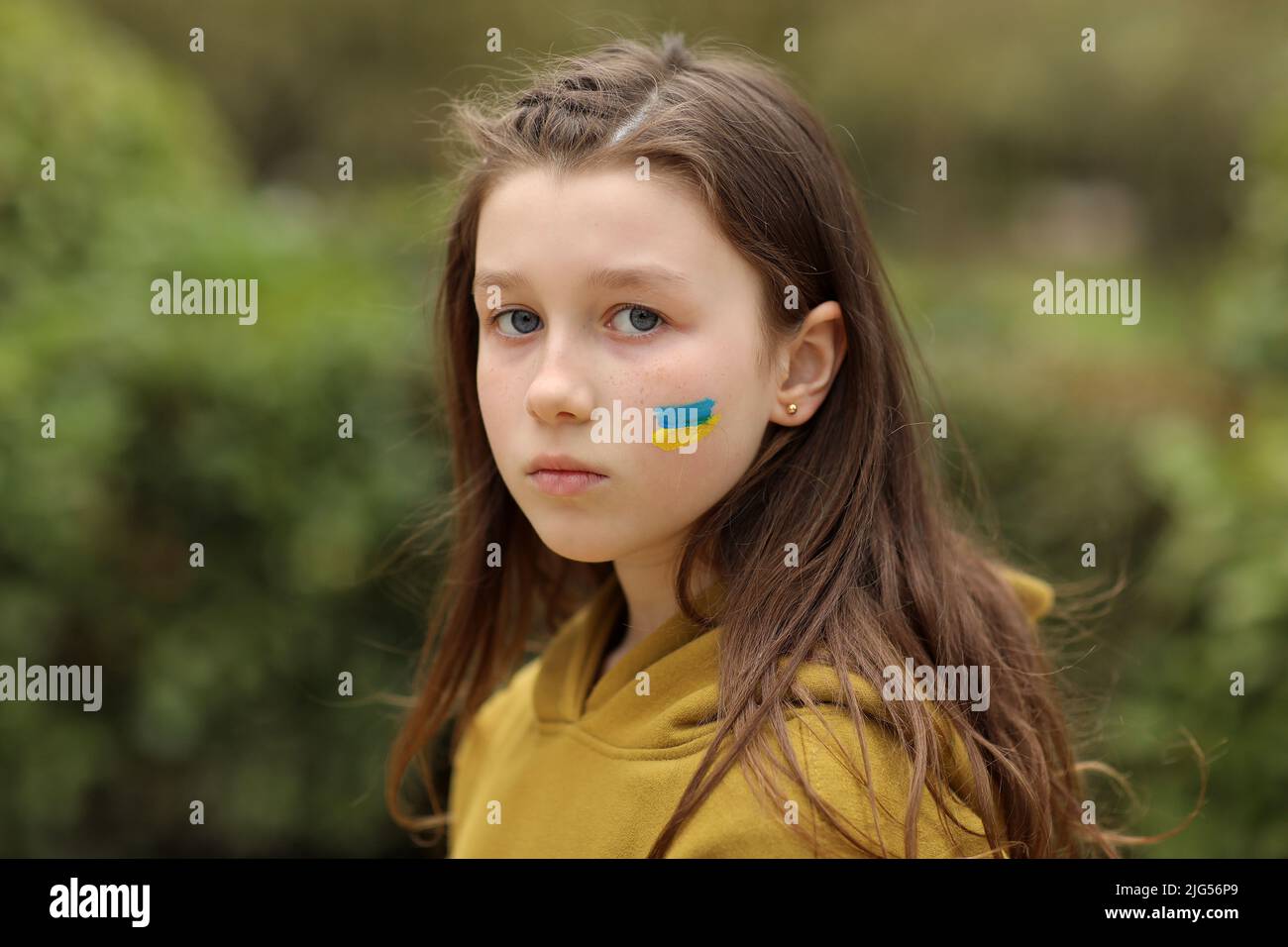 the face of a frightened girl, painted on her cheek in the yellow-blue colors of the Ukrainian flag, a request for help. Children ask for peace. High Stock Photo