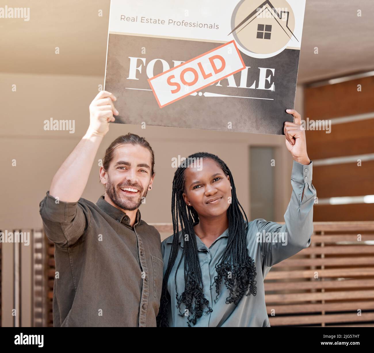We did it. Shot of a young couple holding up a sold board outside their house. Stock Photo