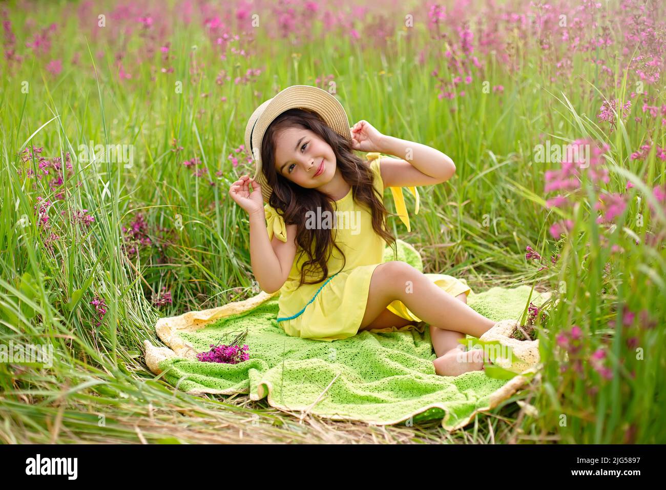 beautiful girl in a straw hat and a yellow dress, sits on a green ...