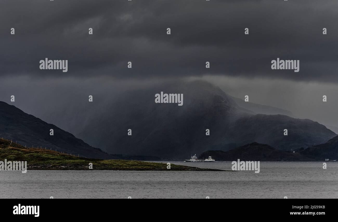 Boat on Loch Linnhe and part of Shuna Island in sunlight; heavy cloud and approaching rain storm rendering background hills as a hazy grey outline. Stock Photo