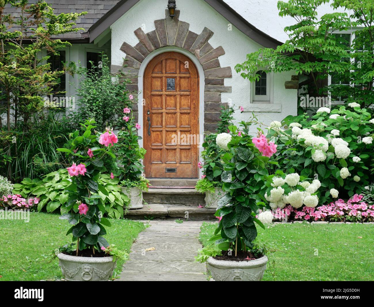 Older house with wood grain front door surrounded by flowers Stock Photo