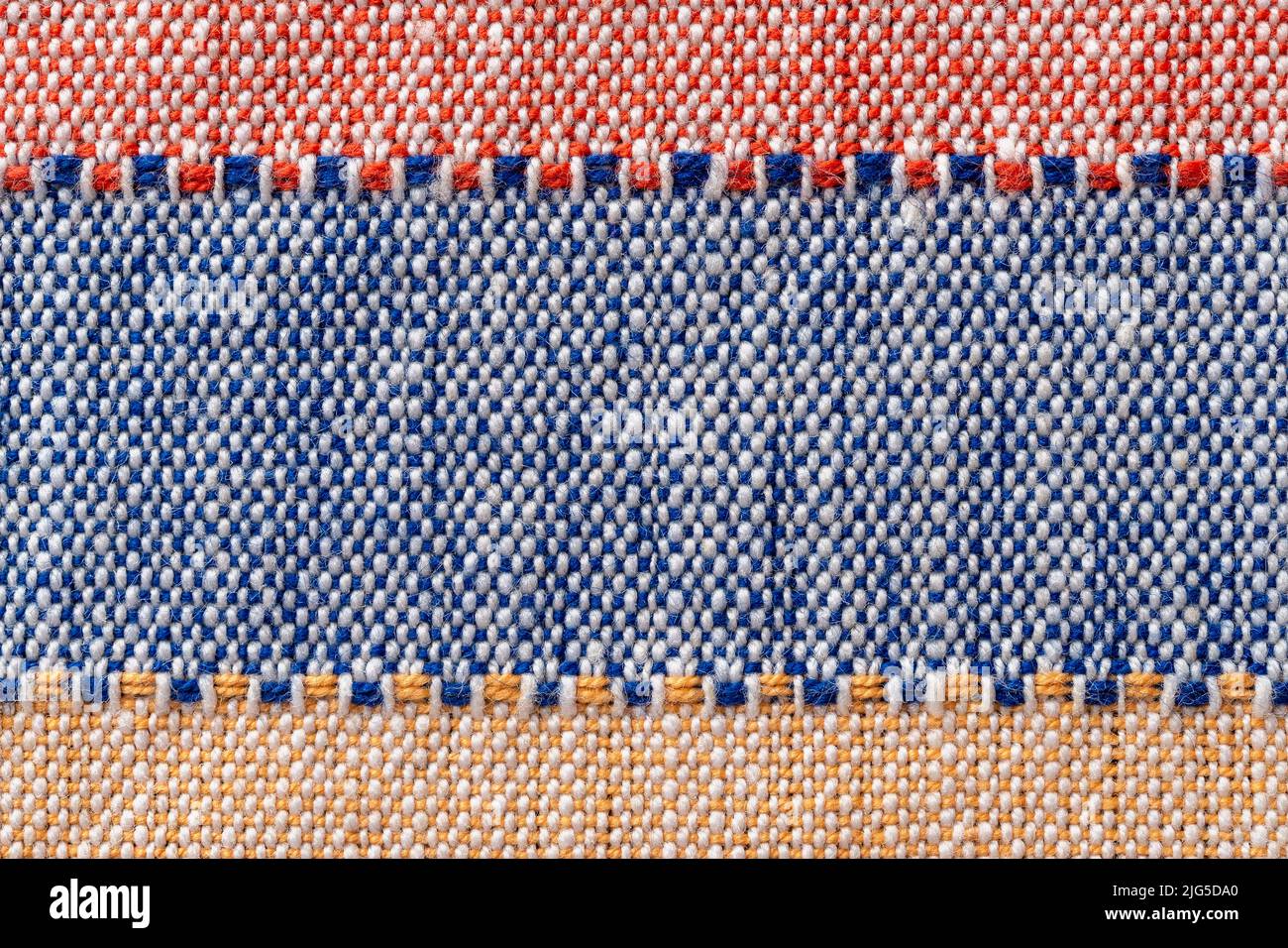 Plain weave fabric macro background. Textile with horizontal strips of red, blue, yellow colors. Detail of cloth texture surface. Weft and warp. Stock Photo