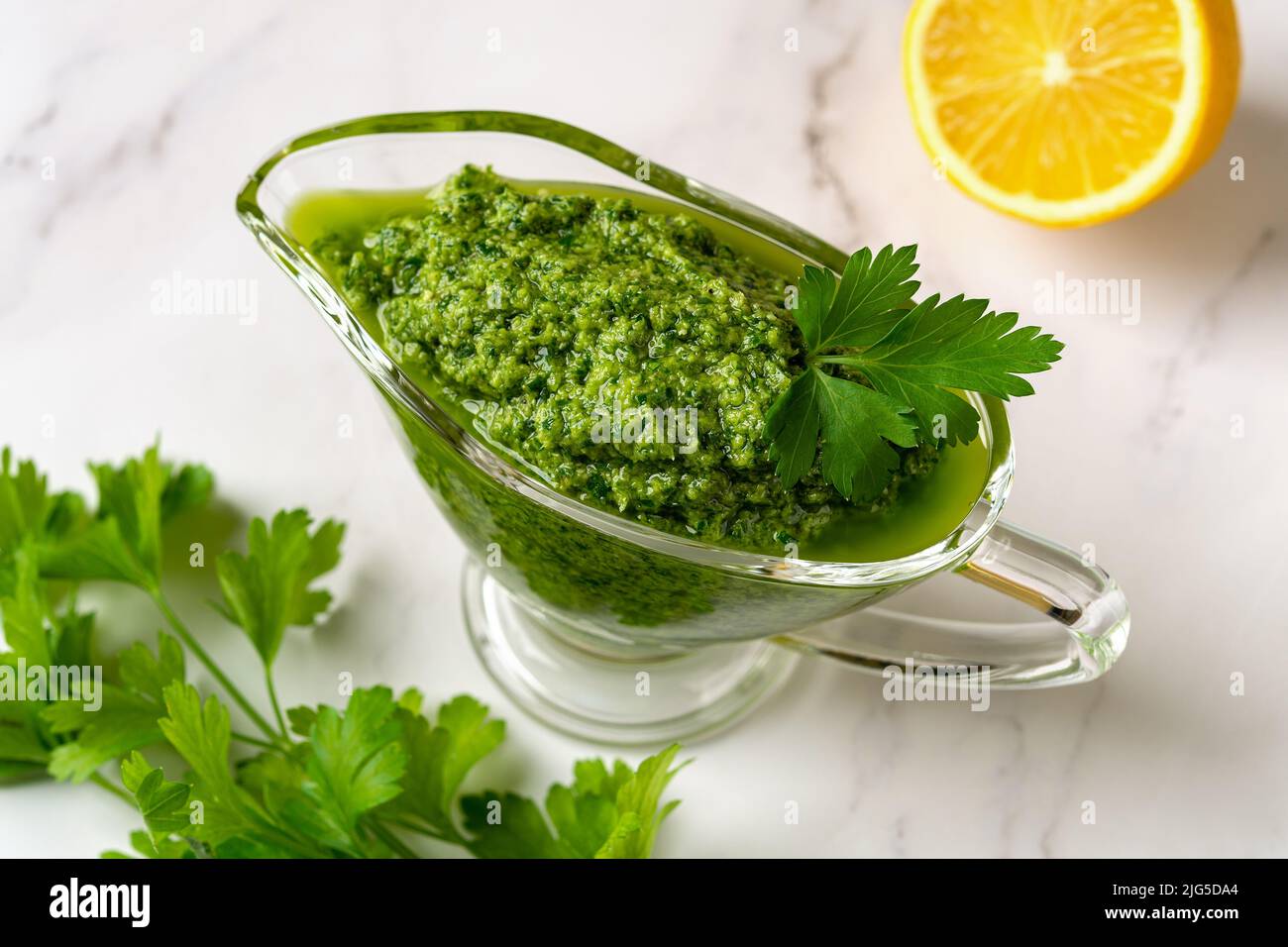Chimichurri dipping sauce in a gravy boat on a table. Green sauce from fresh parsley, garlic cloves, olive oil and lemon juice. Fresh salsa verde. Stock Photo
