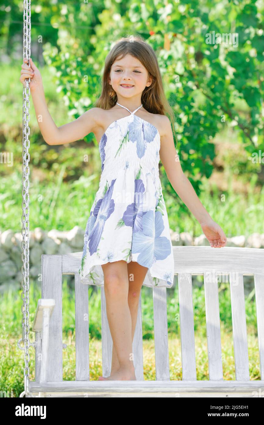 Fashion kids dress. Happy little child girl on a swing in the summer park.  Happy kid having fun outdoors Stock Photo - Alamy