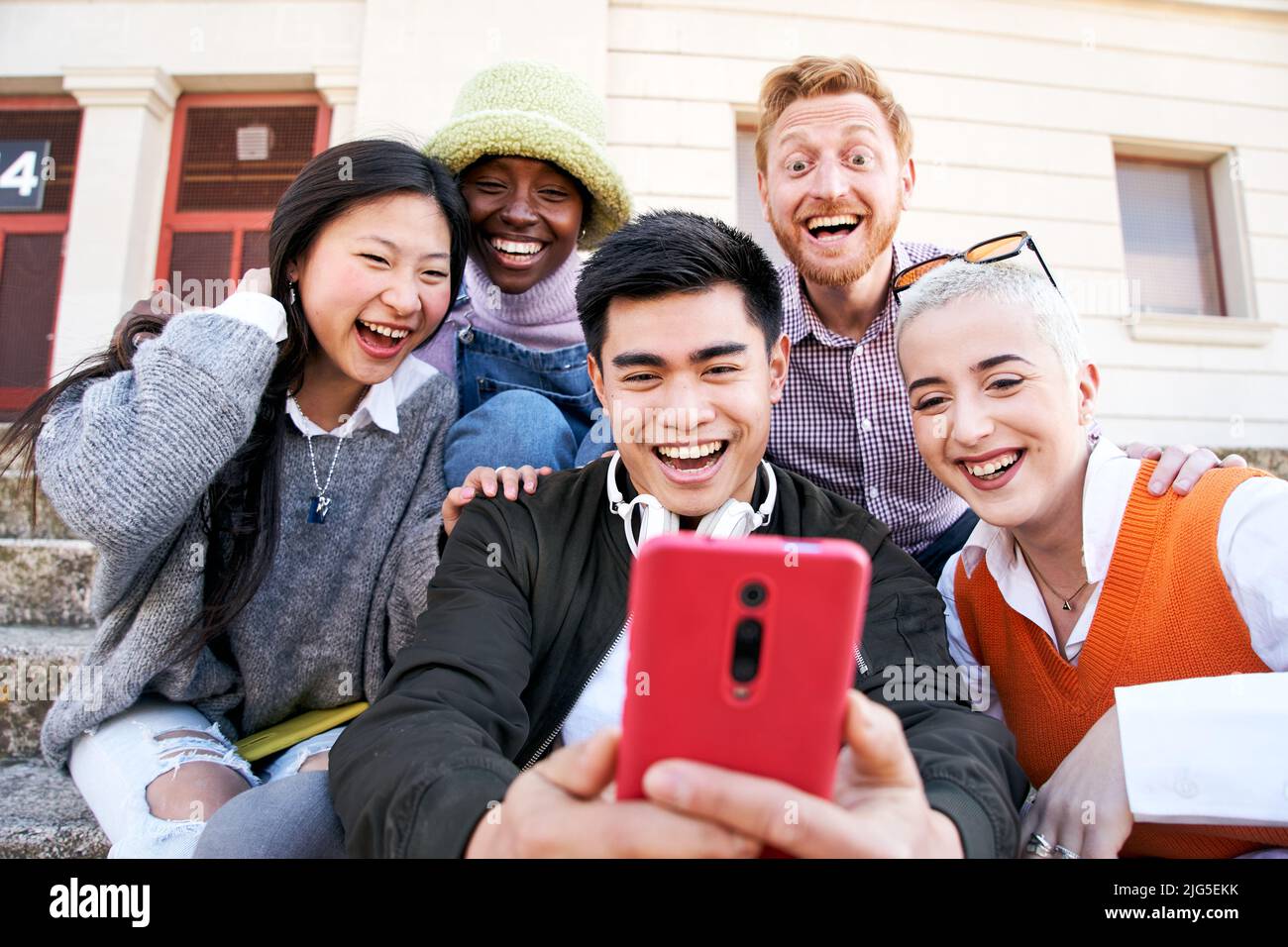 Group of Smiling people using mobile phone outdoors. Cheerful guys and girls friends having fun watching something at digital display. Happy vacations Stock Photo