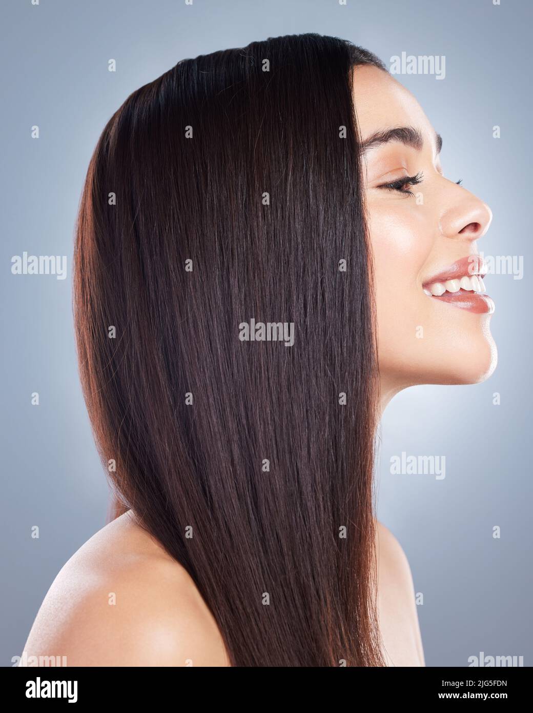 Profile view of a beautiful brown-haired woman with smooth and shiny hair posing against a grey background. Happy young brunette woman with beautiful Stock Photo