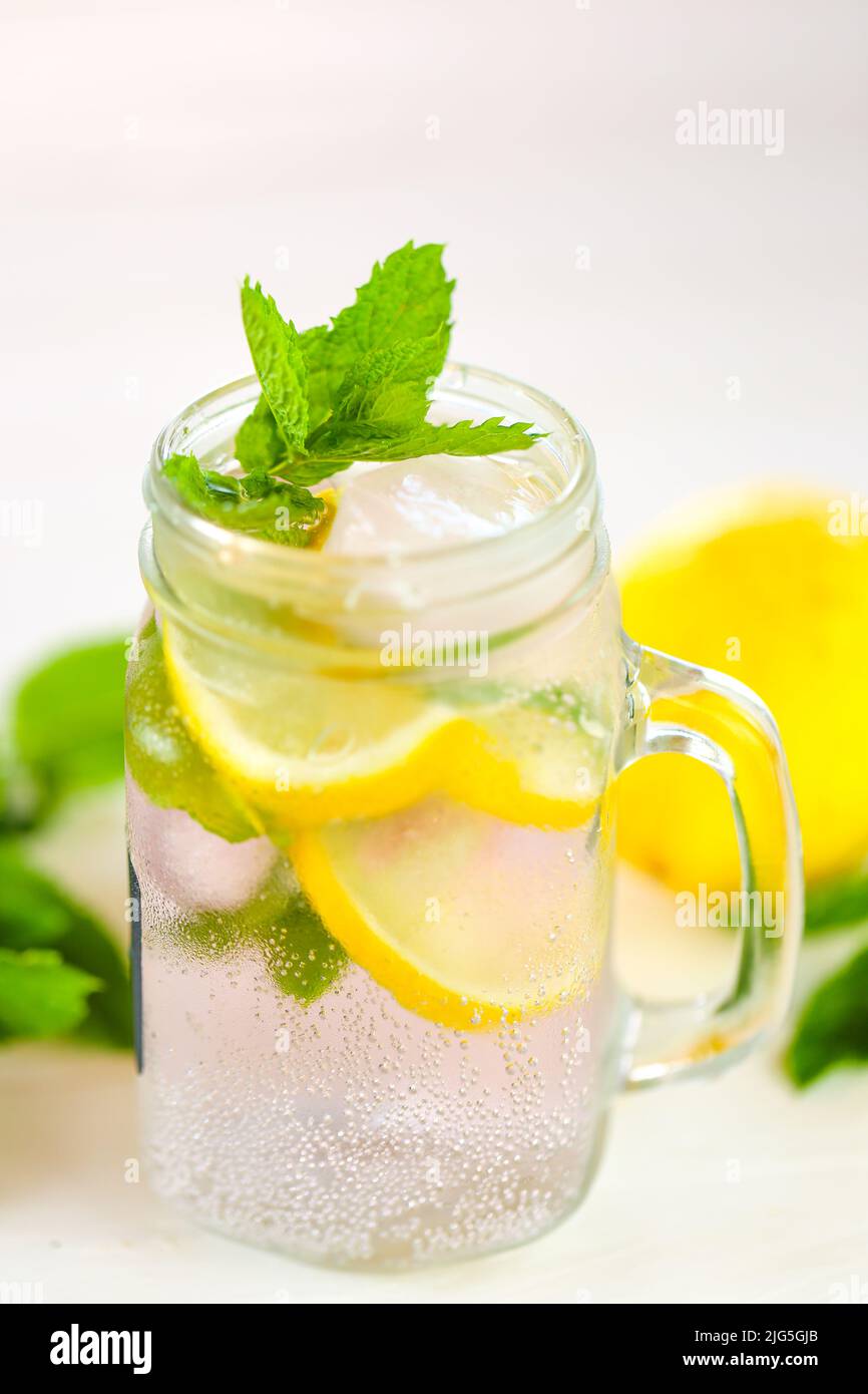 Lemon water with ice.Citrus cocktail with mints. Sassy lemon water.Lemon summer drink.Dietary lemon drink. ice falls into a glass with a cocktail Stock Photo