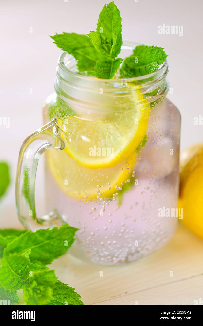 cocktail with mint leaves. Sassy lemon water.Lemon summer drink.Dietary lemon drink. ice falls into a glass with a cocktail.Sprig of mint in a glass Stock Photo