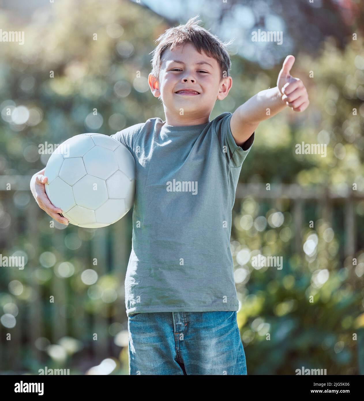 Good job, I turned out perfectly. Shot of an adorable little boy showing the thumbs up while holding a soccer ball outside. Stock Photo