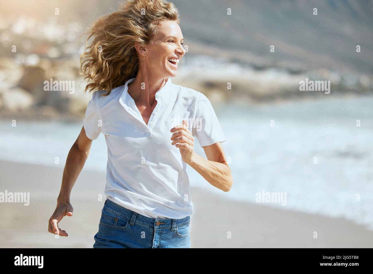 Cheerful mature woman running on the beach on a sunny day. Beautiful
