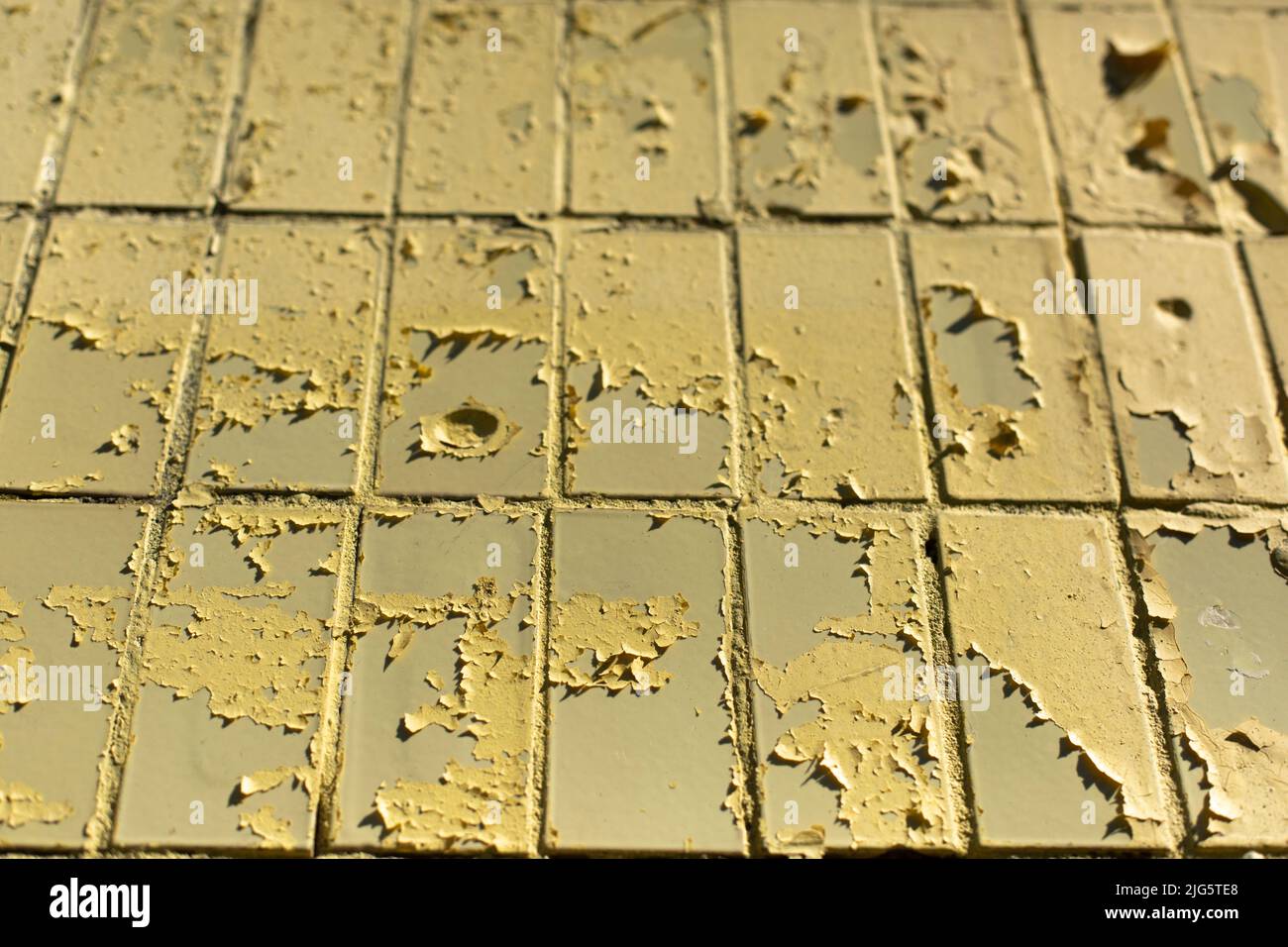 Texture of old tile wall. Yellow paint crumbled. Paint on top of tiles