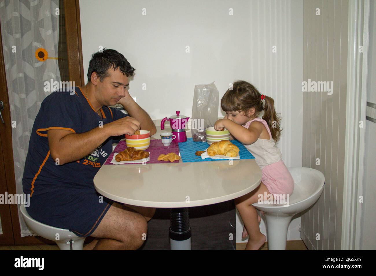 Image of a young dad with his daughter still sleepy while having breakfast in the morning dipping cookies in milk. The right motivation and energy to Stock Photo