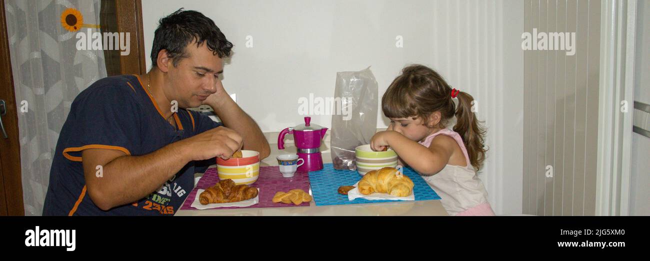 Image of a young dad with his daughter still sleepy while having breakfast in the morning dipping cookies in milk. The right motivation and energy to Stock Photo