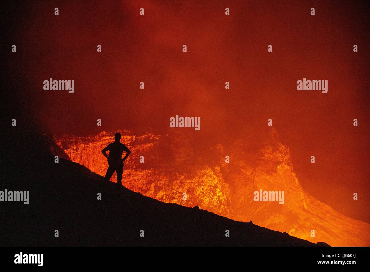 An explorer poses by the crater rim edge as he looks into the Murum vent, on Ambrym island in Vanuatu, during an expedition to map the crater. Stock Photo