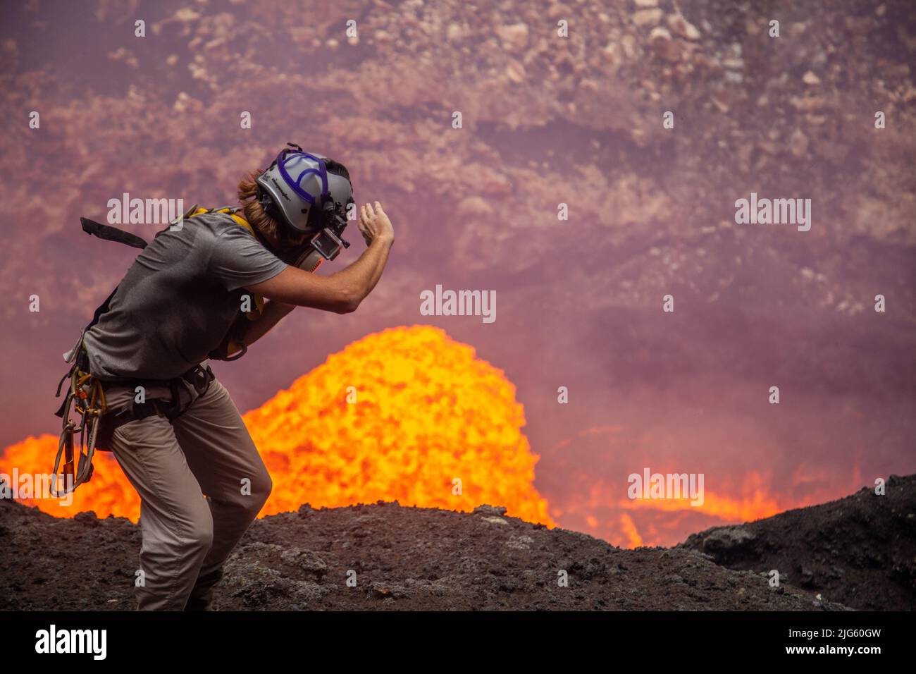 An explorer tries to protect his face from the extreme heat escaping from a lava burst coming out of the lava lake inside the Marum vent on Ambrym isl Stock Photo