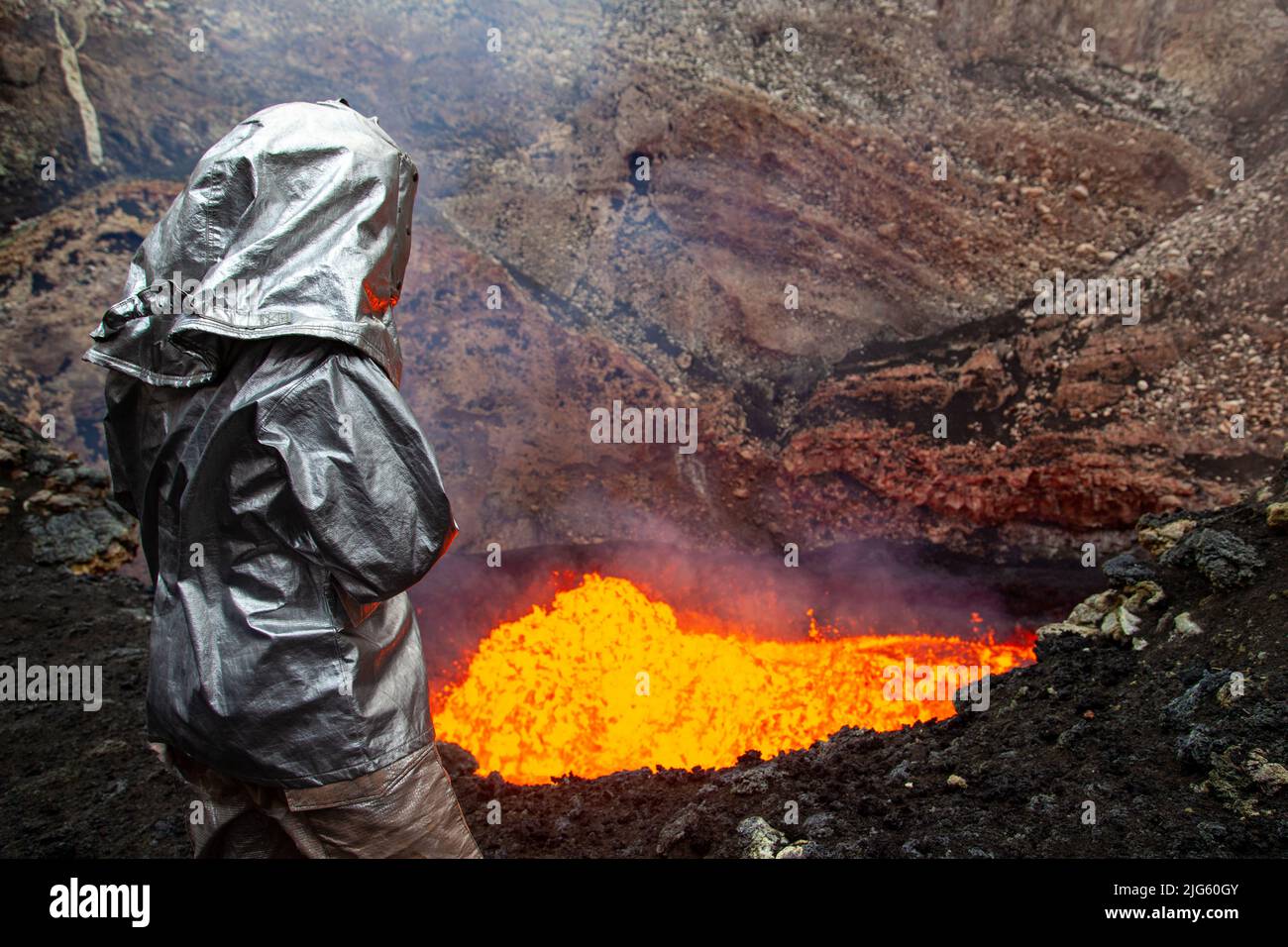 An explorer wearing a heat proximity suit stares into the lava lake inside the Marum crater during an expedition to the Ambrym volcano in Vanuatu. Stock Photo