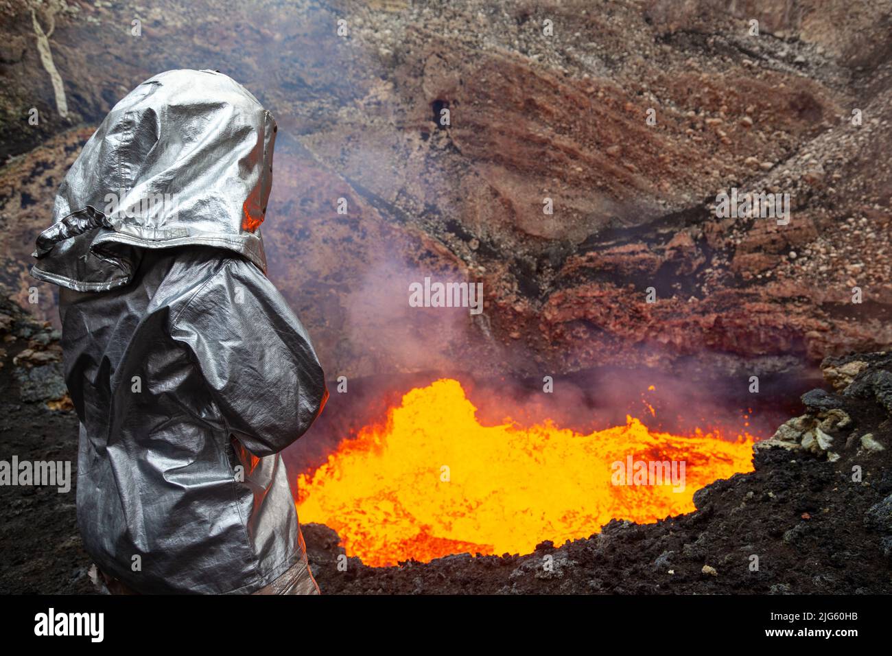 An explorer wearing a heat proximity suit stares into the lava lake inside the Marum crater during an expedition to the Ambrym volcano in Vanuatu. Stock Photo