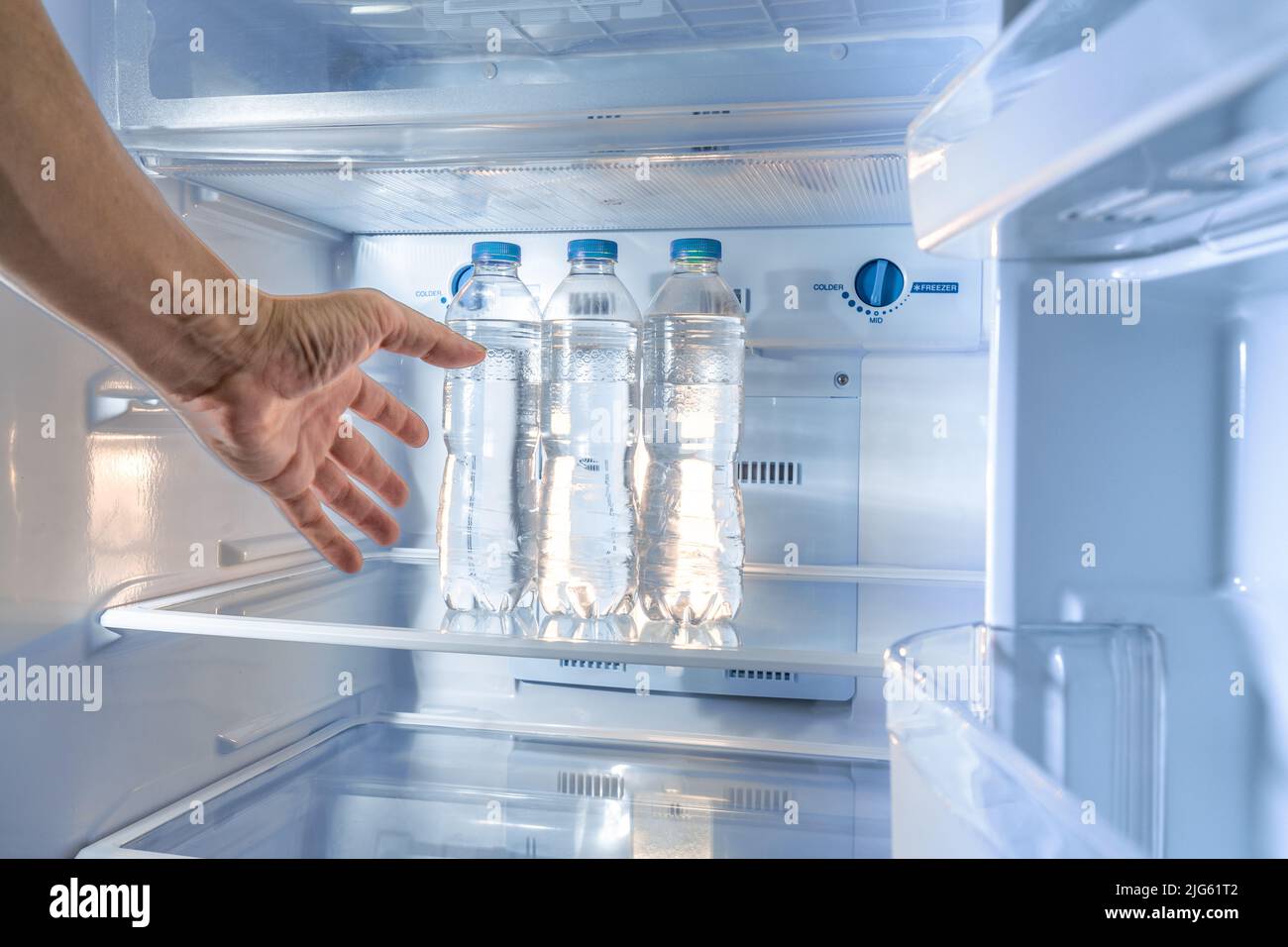 A shaky thirsty male's hand reaching out to grab a cold water bottle from a refrigerator, with motion blur effect added to the hand Stock Photo