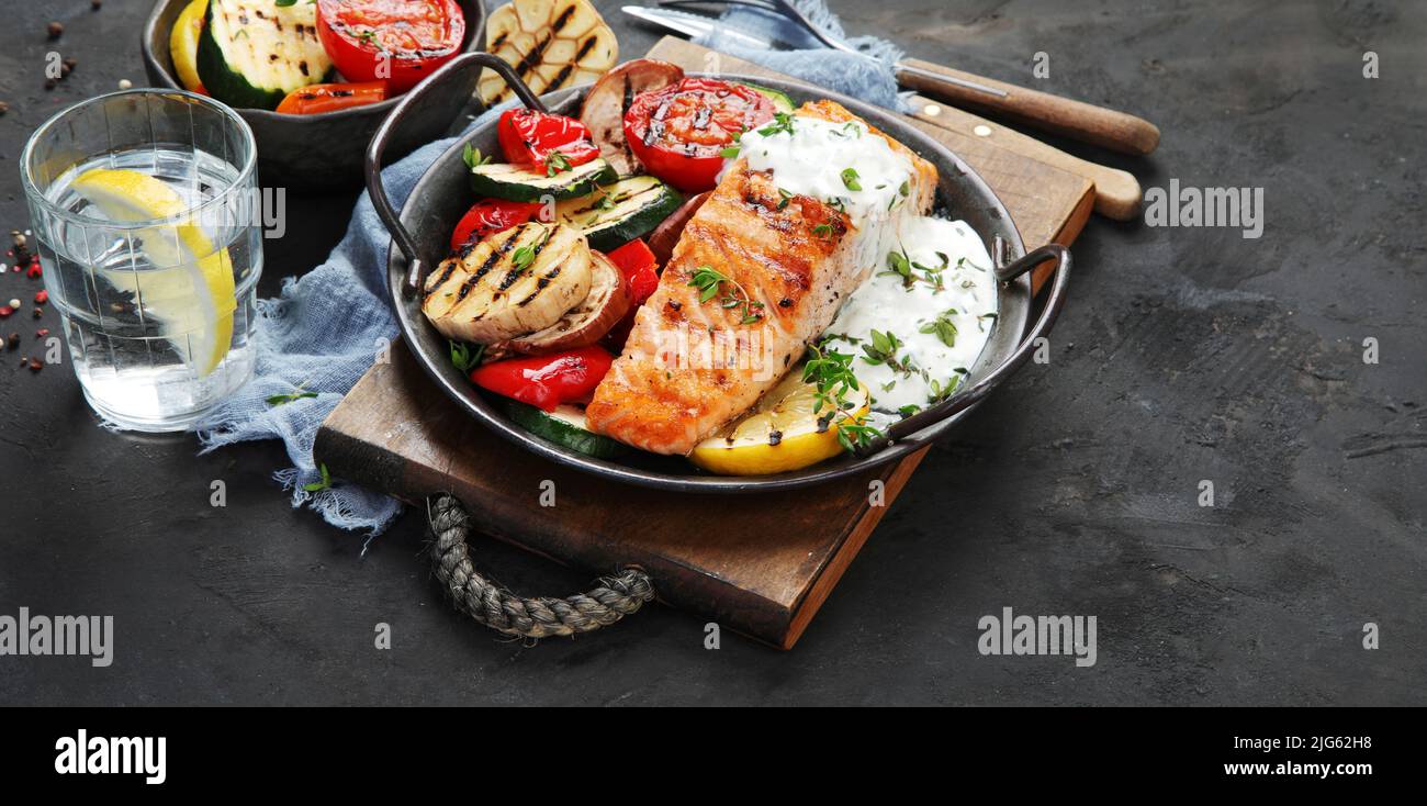 Salmon steak with vegetables and white sauce on dark background ...