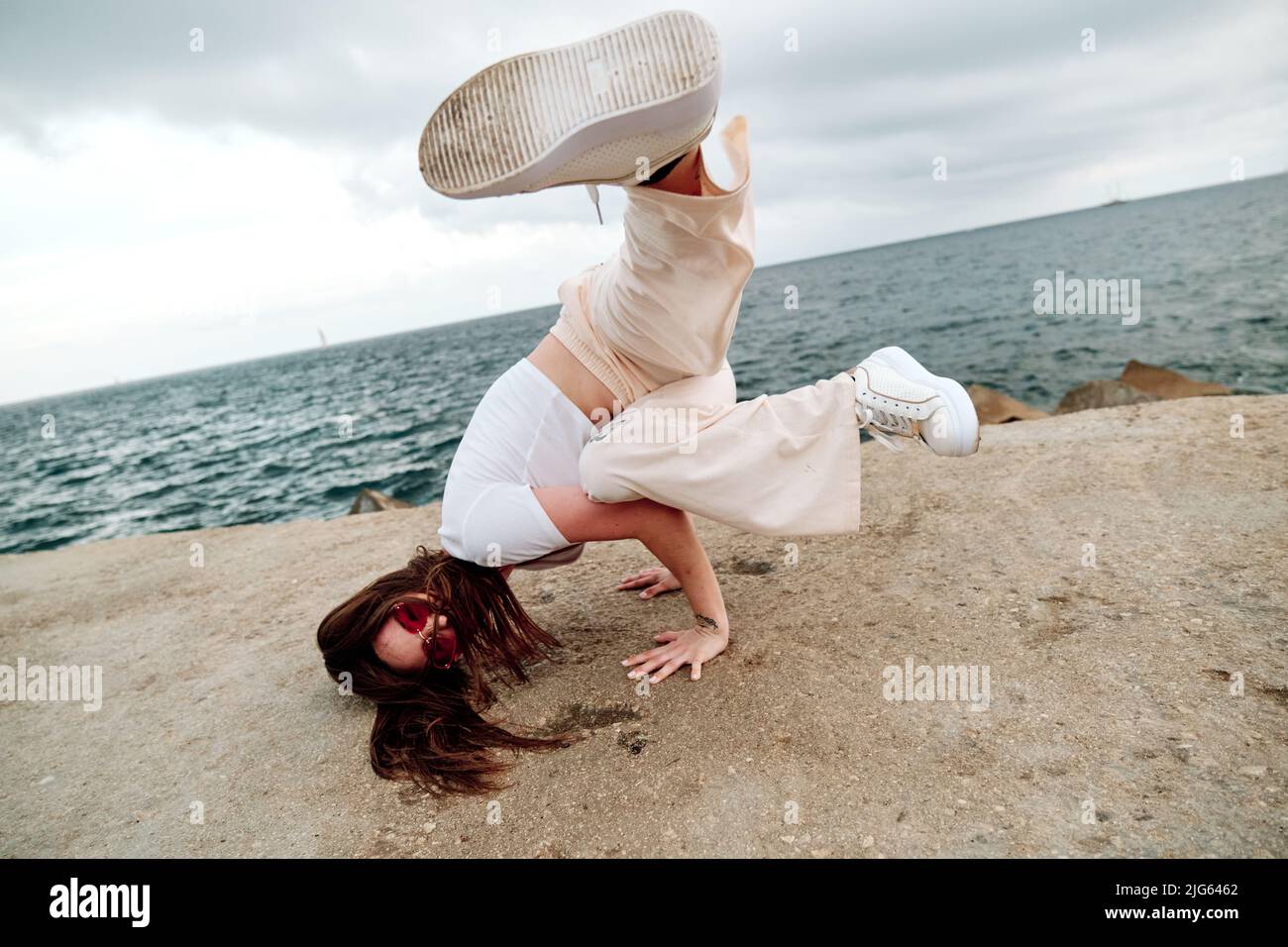 Female dancer doing handstand while breakdancing outdoors against sea. Stock Photo