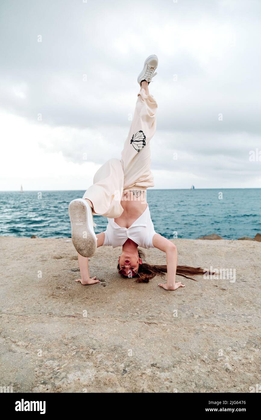 Breakdance dancer doing a handstand outdoors near the sea. Stock Photo