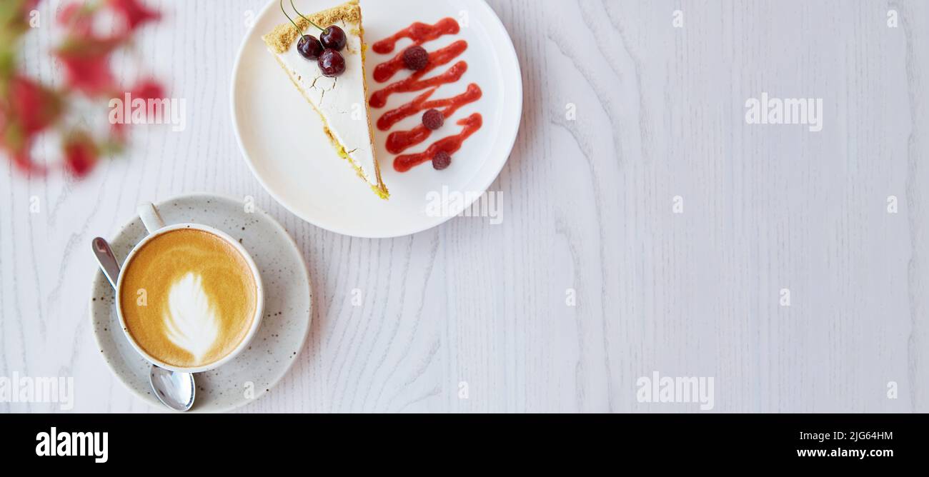 Cherry, raspberry biscuit cake and cup of cappuccino on wooden table