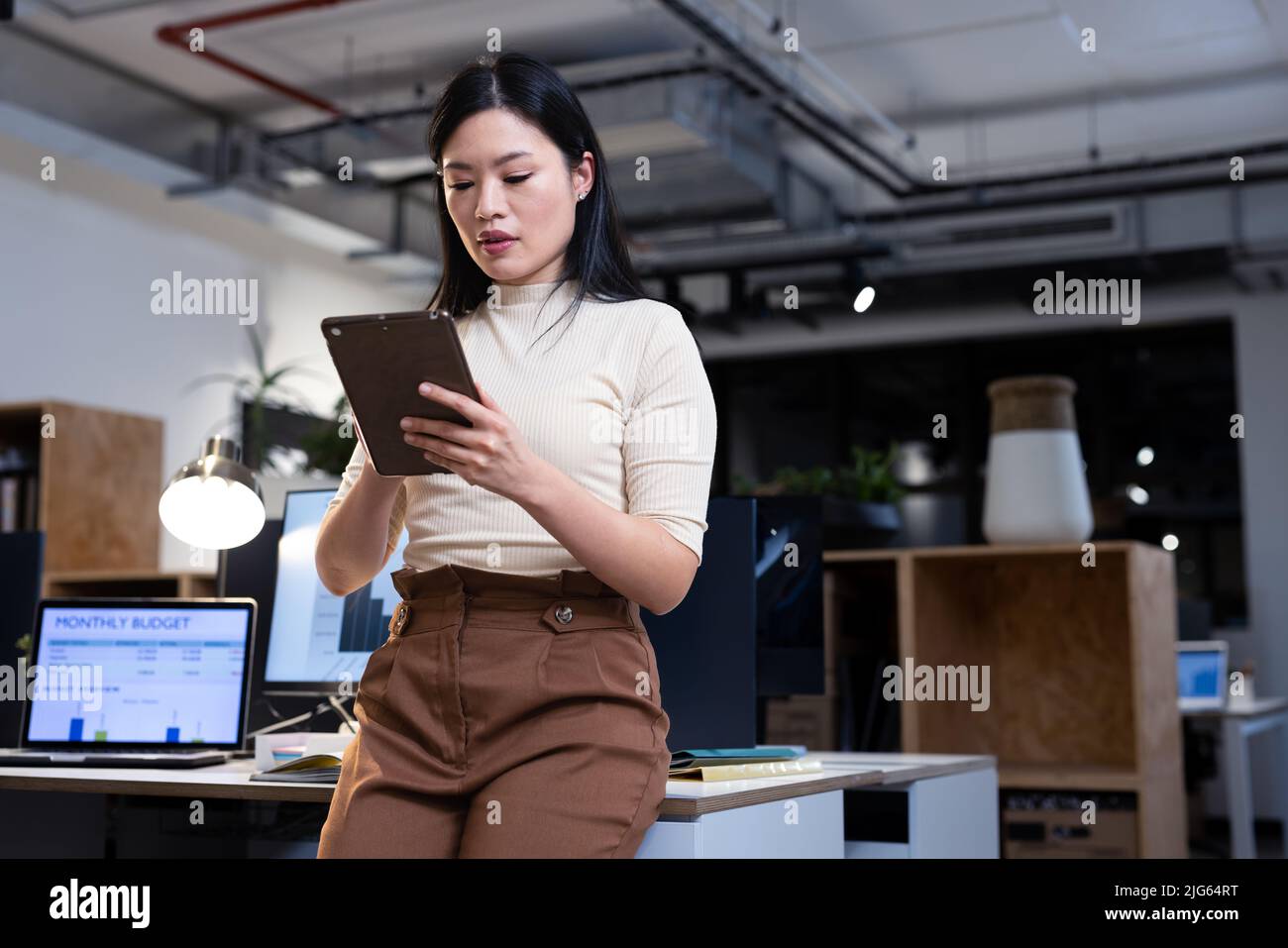 Low angle view of female asian professional working over digital pc while leaning on desk at night Stock Photo