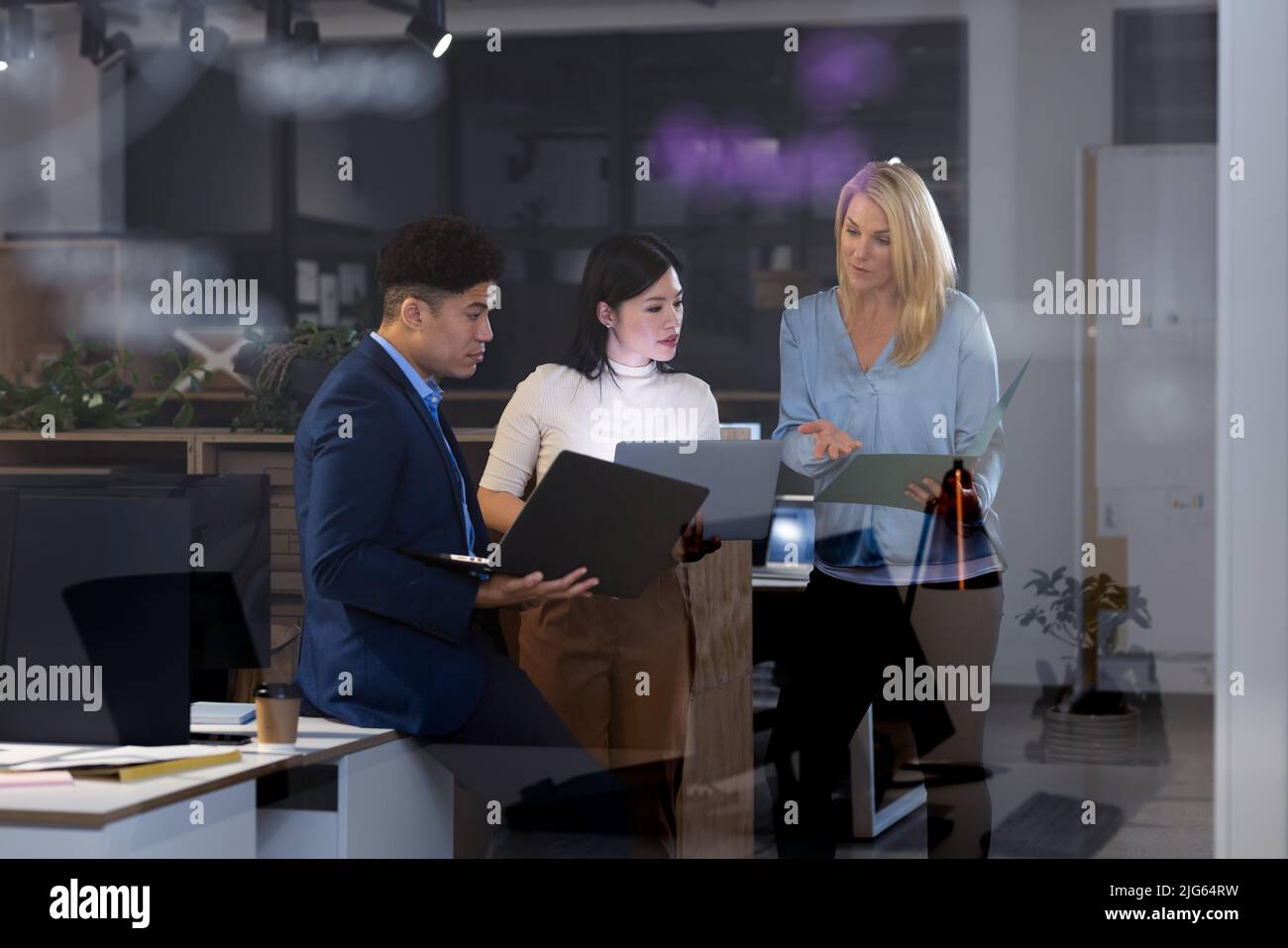 Multiracial coworkers analyzing data with laptops and report while working late in office at night Stock Photo