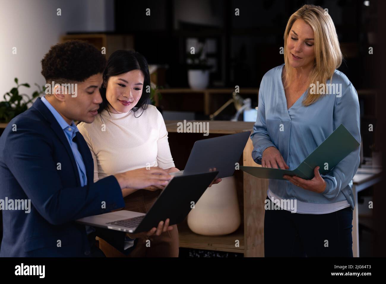 Multiracial colleagues with laptops and report analyzing data and brainstorming in office at night Stock Photo