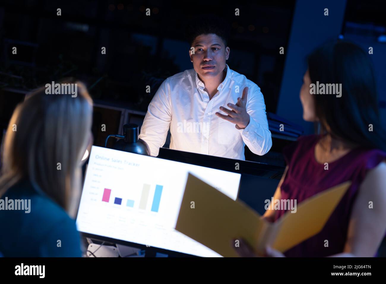 Multiracial businessman discussing with female workers while working late in modern office at night Stock Photo