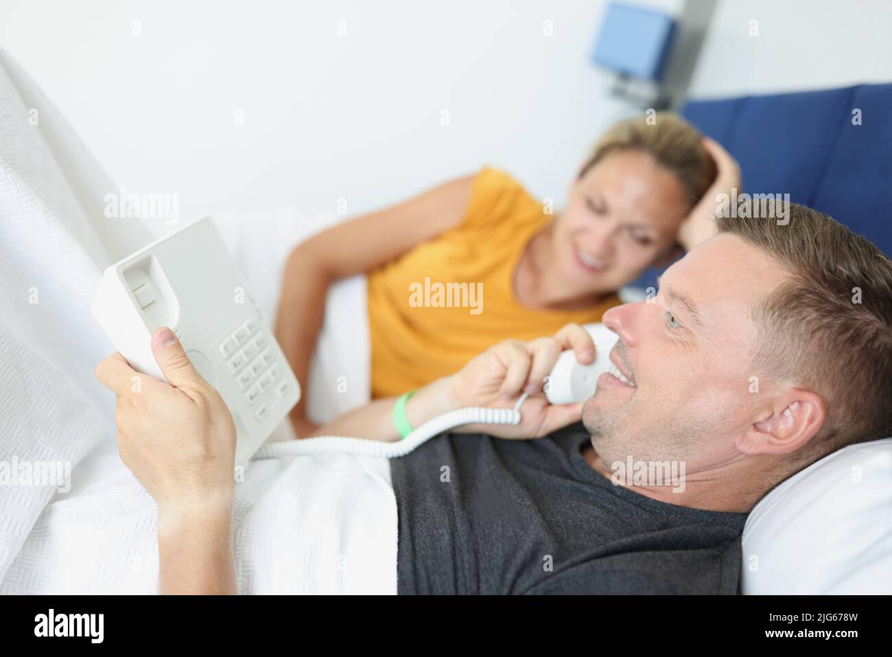 Happy couple lying in bed and making order using hotel phone Stock Photo