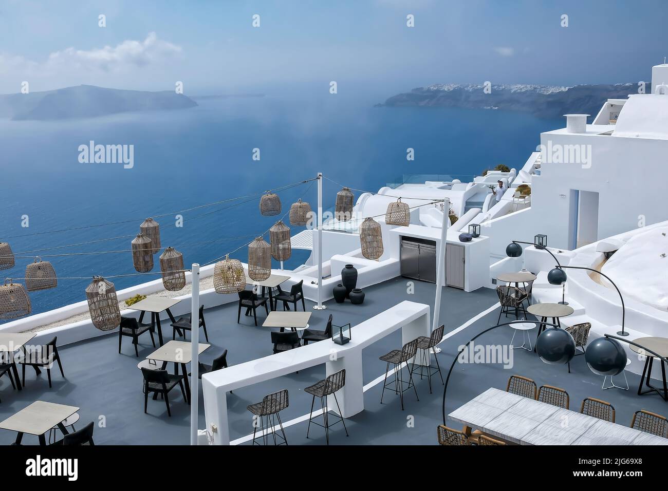 Santorini, Greece - May 13, 2021 :  View of a picturesque terrace decorated with tables, chairs  and lights overlooking  the Aegean Sea on a sunny day Stock Photo