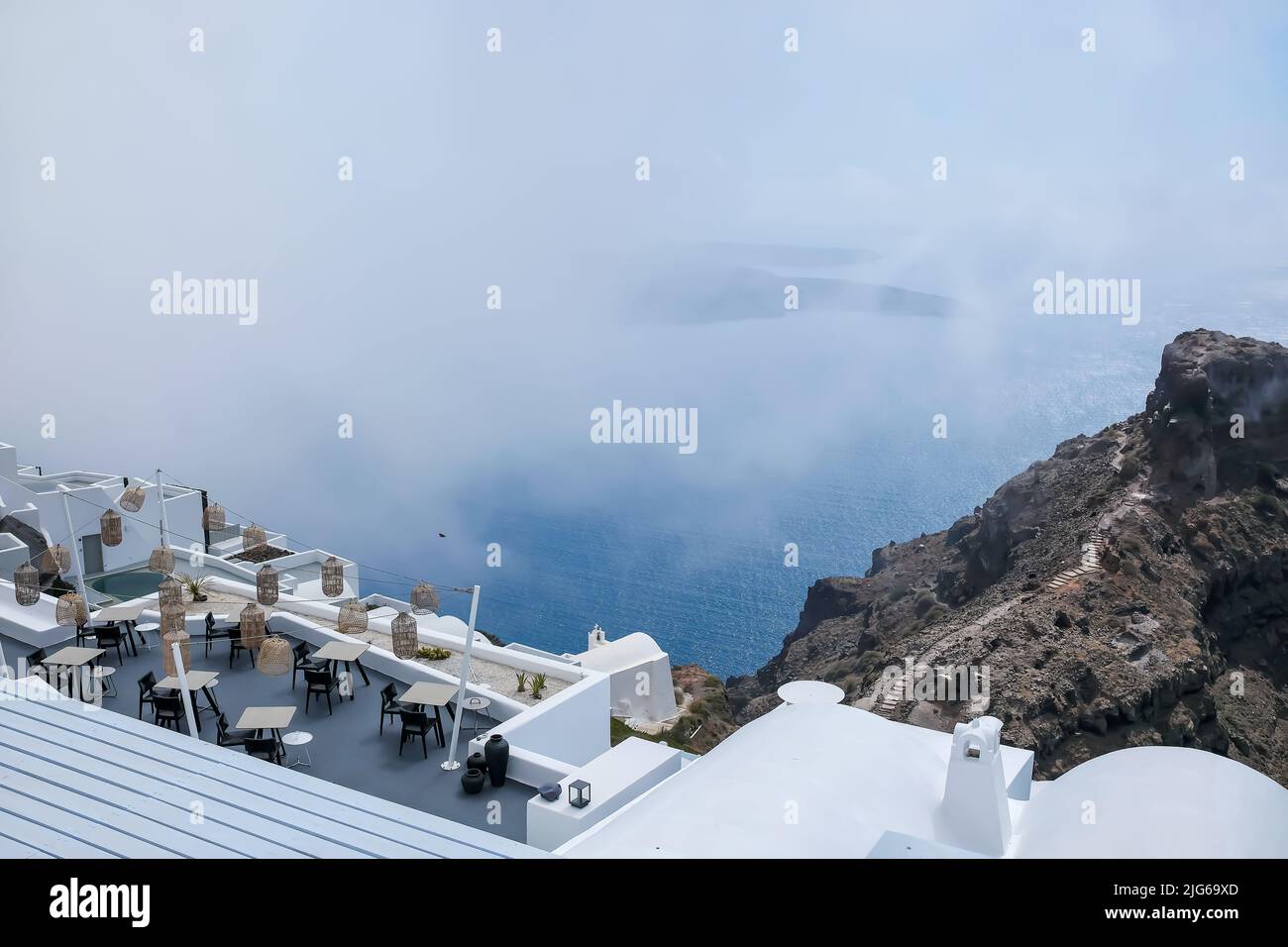 Santorini, Greece - May 13, 2021 :  View of a picturesque terrace decorated with tables, chairs  and lights overlooking  the Aegean Sea on a cloudy day Stock Photo