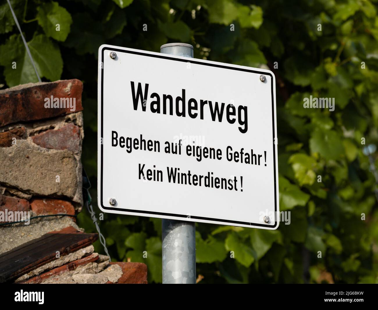Wanderweg (hiking trail) sign in the nature. The text in German language says the use of the footpath is at one's own risk without winter clearance. Stock Photo