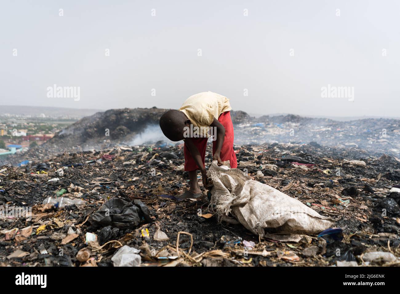 Young boy at a smoky African landfill collecting valuable items for resale, surrounded by clouds of smoke Stock Photo