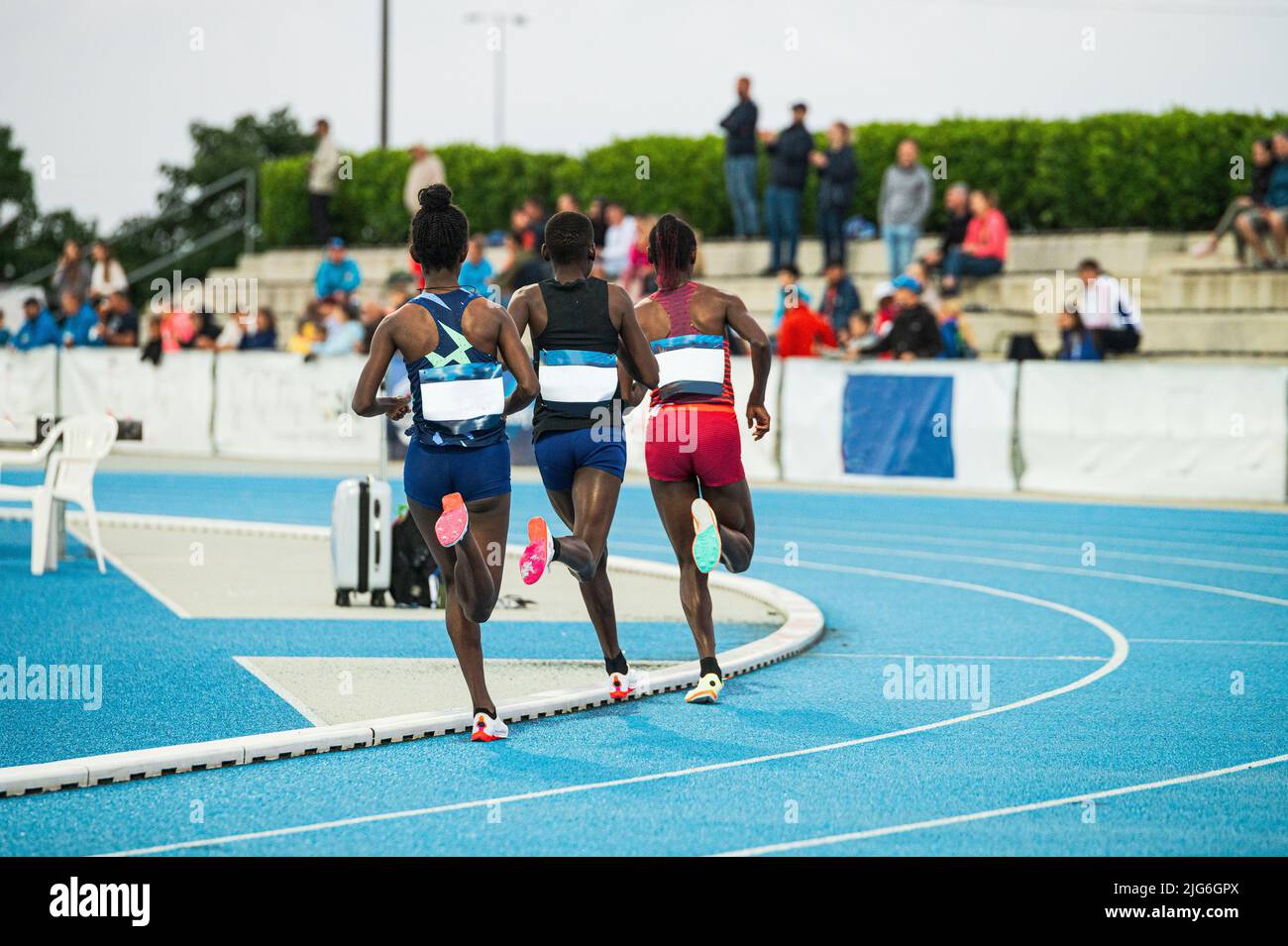 Three female endurance runners race on a blue track. Track and field ...