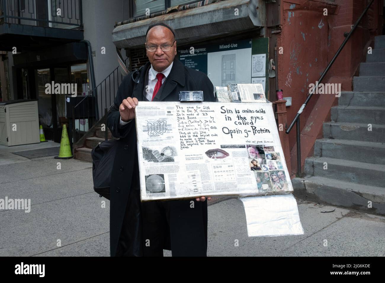 An eccentric man wearing a skullcap and holding handmade signs with theories about health, religion, God and Satan. In Brooklyn, New York. Stock Photo
