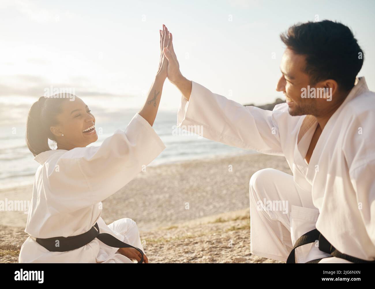 Concluding another successful sunset session. Shot of two young martial artists giving each other a high five while practicing karate on the beach. Stock Photo