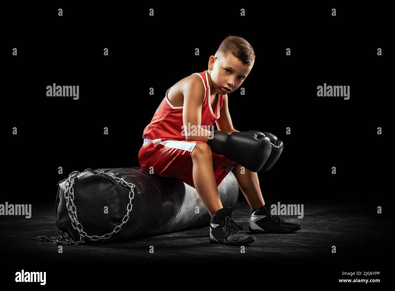 Young beginner boxer, sportive boy training isolated over dark